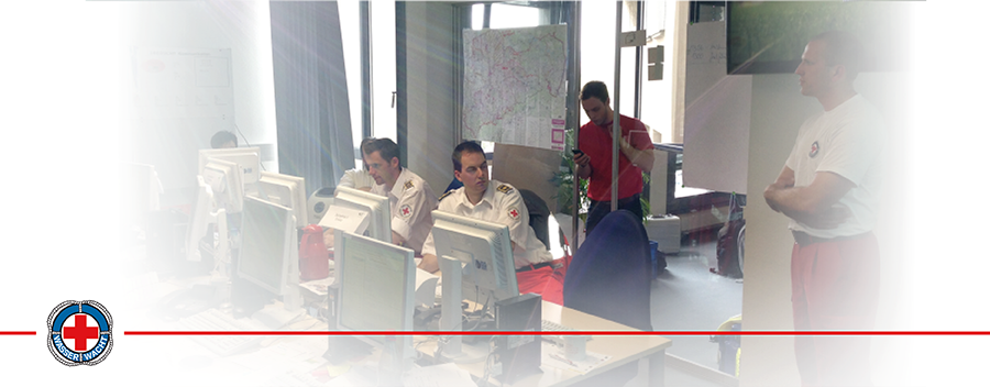Mehrere Ehrenamtliche der Wasserwacht stehen und sitzen in einem großen Büro. Einige arbeiten an Computern, während andere Karten an Tafeln untersuchen.