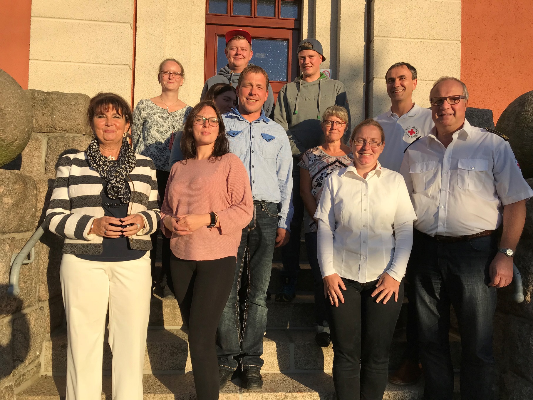 Die Mitglieder der Wasserwacht der Ortsgruppe Hartmannsdorf stehen vor dem Eingang eines Gebäudes und schauen in die Kamera.